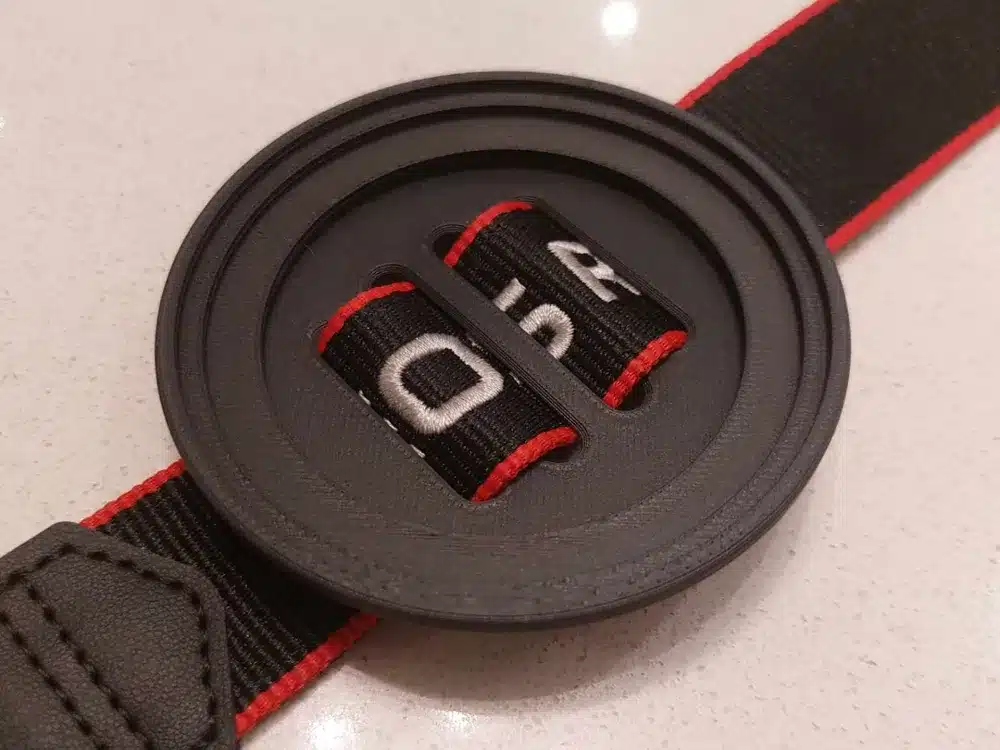 Black camera lens cap attached to a black and red strap on a light surface.