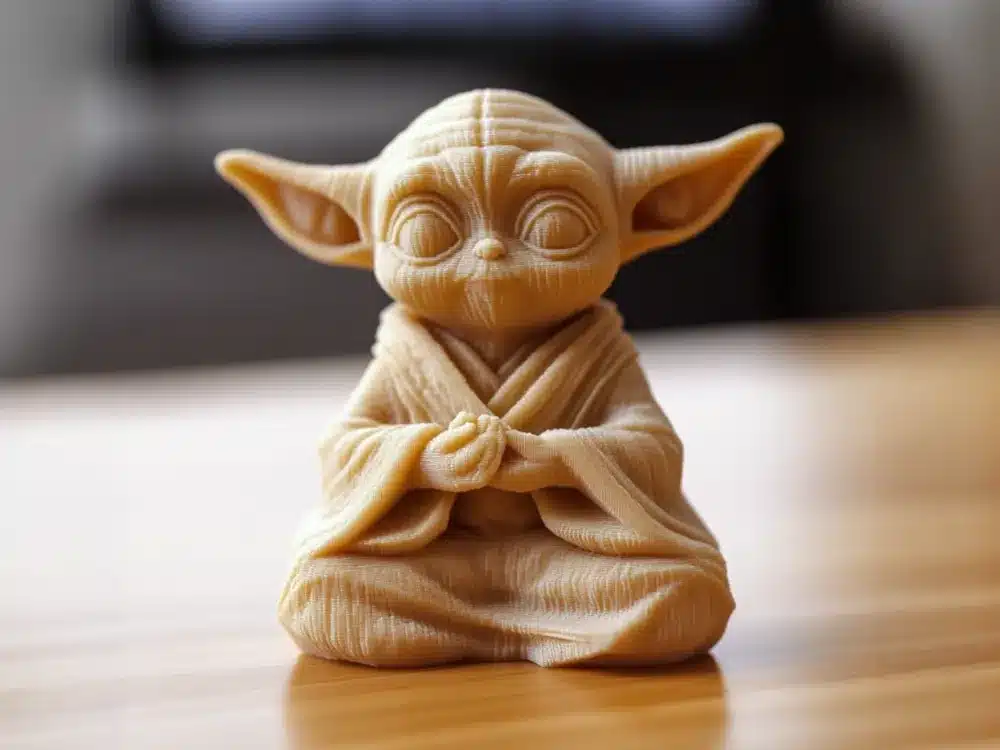 3D-printed Yoda figurine in meditation pose on wooden surface, detailed craftsmanship.
