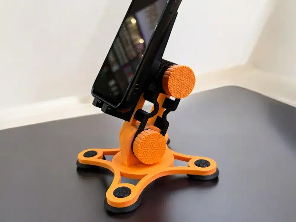 Orange 3D-printed phone stand holding a smartphone on a black surface. Perfect for ergonomic device use.