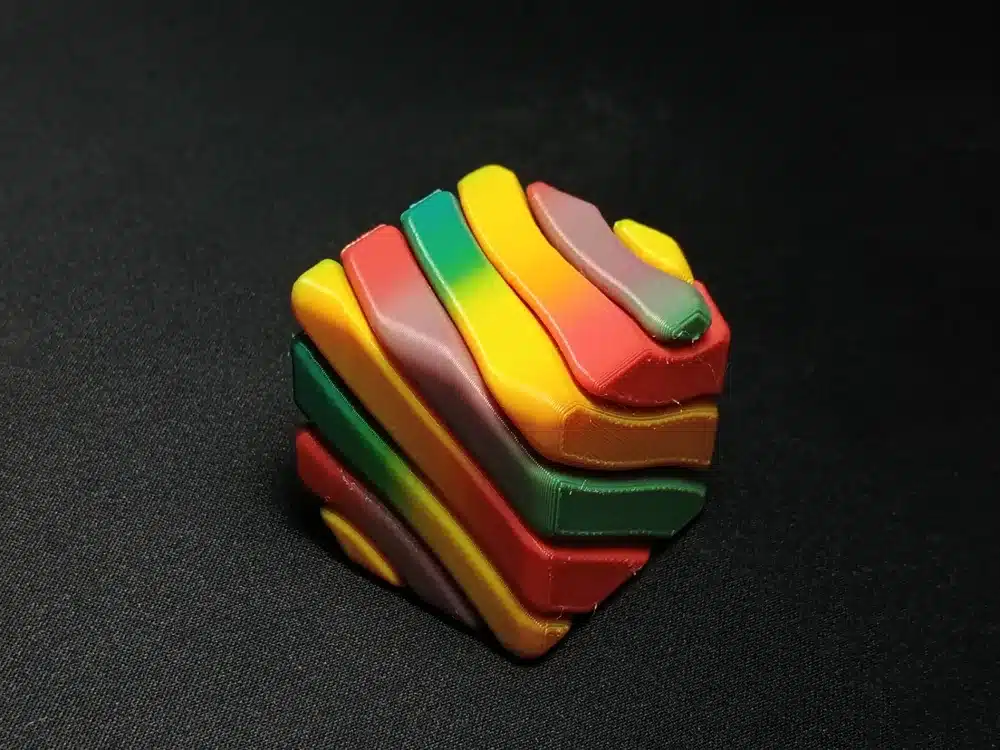 Colorful twisted cube puzzle on black background, showing vibrant layers of yellow, orange, green, and red.