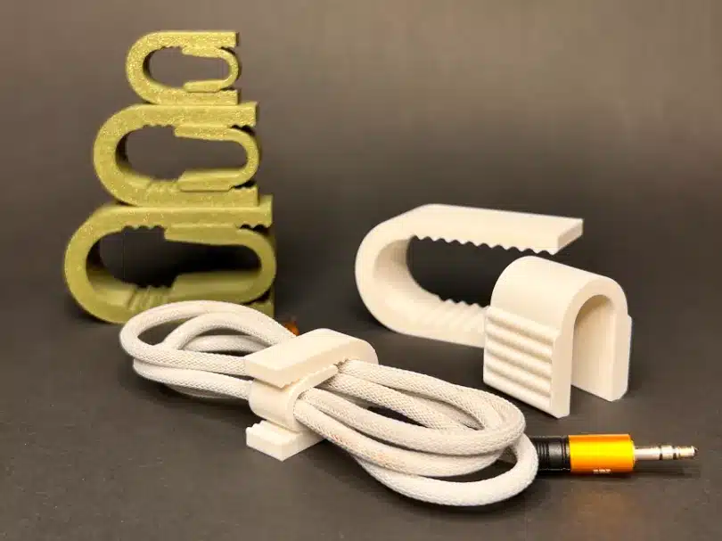 3D-printed cable organizers in gray and white with a coiled cable and audio jack on a dark background.