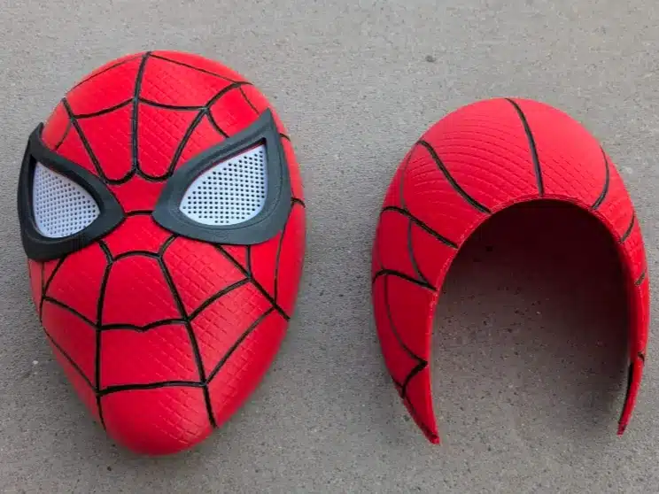 Red superhero mask with web design, split into front and back pieces on a gray surface.