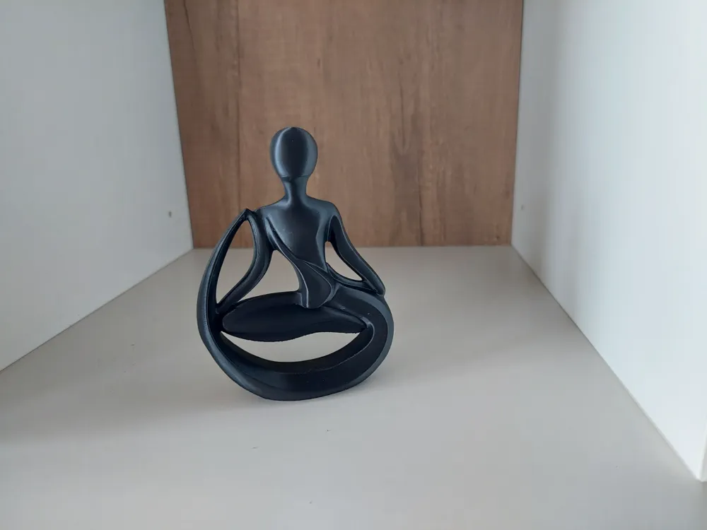 Minimalist black sculpture of a person sitting in a meditative yoga pose on a white and wooden shelf.