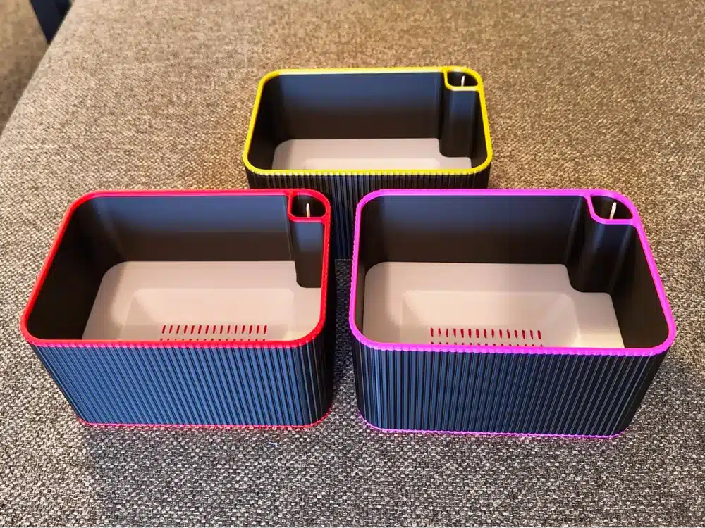 Three colorful rectangular storage bins on a textured surface, featuring pink, red, and yellow trim designs.