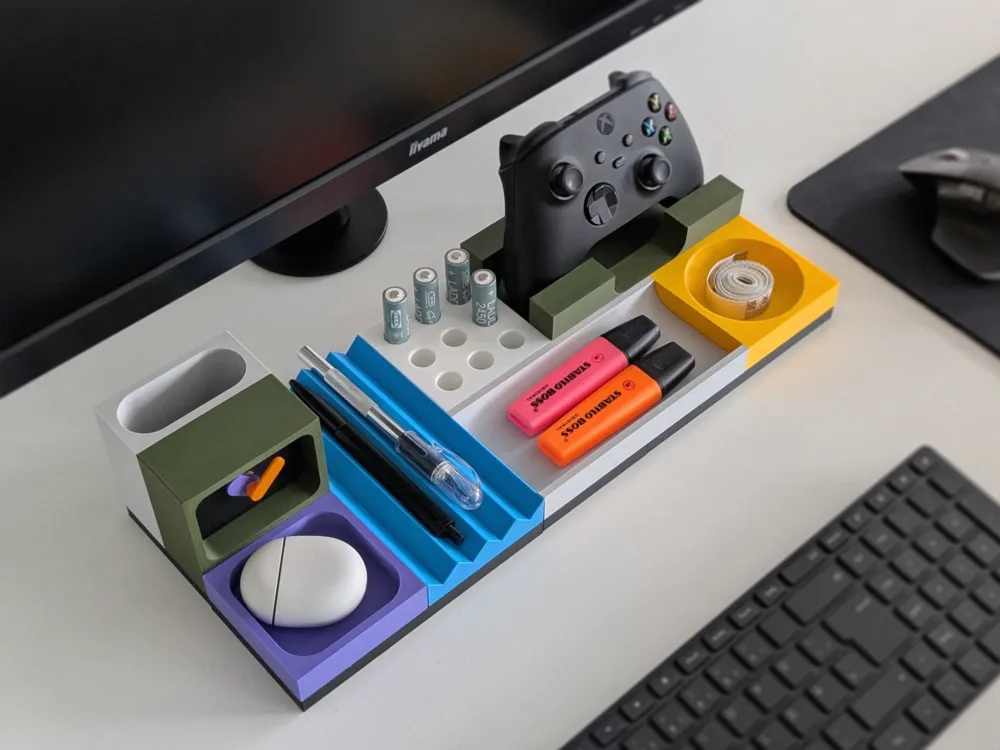 Organized desk with colorful stationery holder, computer mouse, pens, and a game controller near a keyboard and monitor.