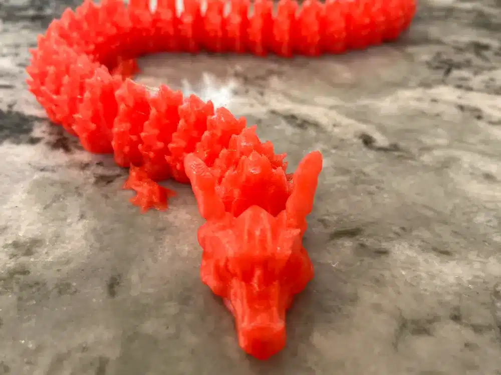 Red 3D-printed dragon on a marble surface, showcasing intricate details and flexible structure.