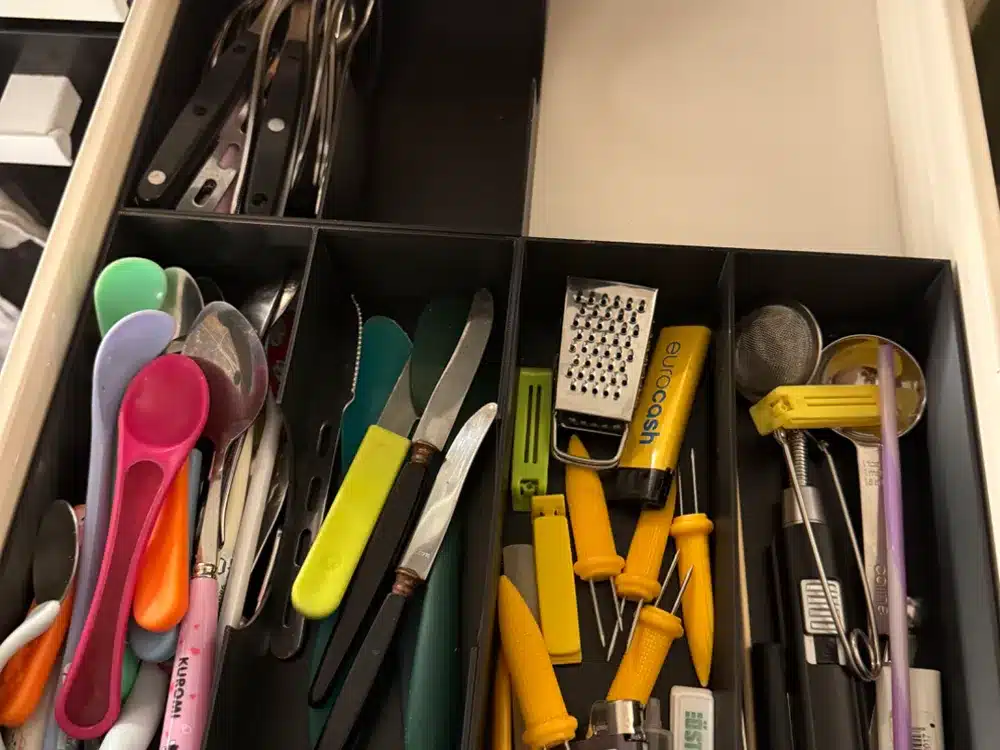 Kitchen drawer with assorted colorful utensils, including spoons, knives, and kitchen gadgets in separate compartments.