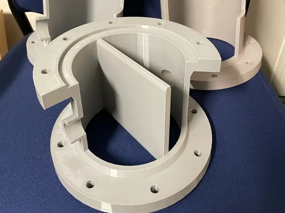 3D printed gray plastic components on a blue surface, showcasing circular design and precision engineering.