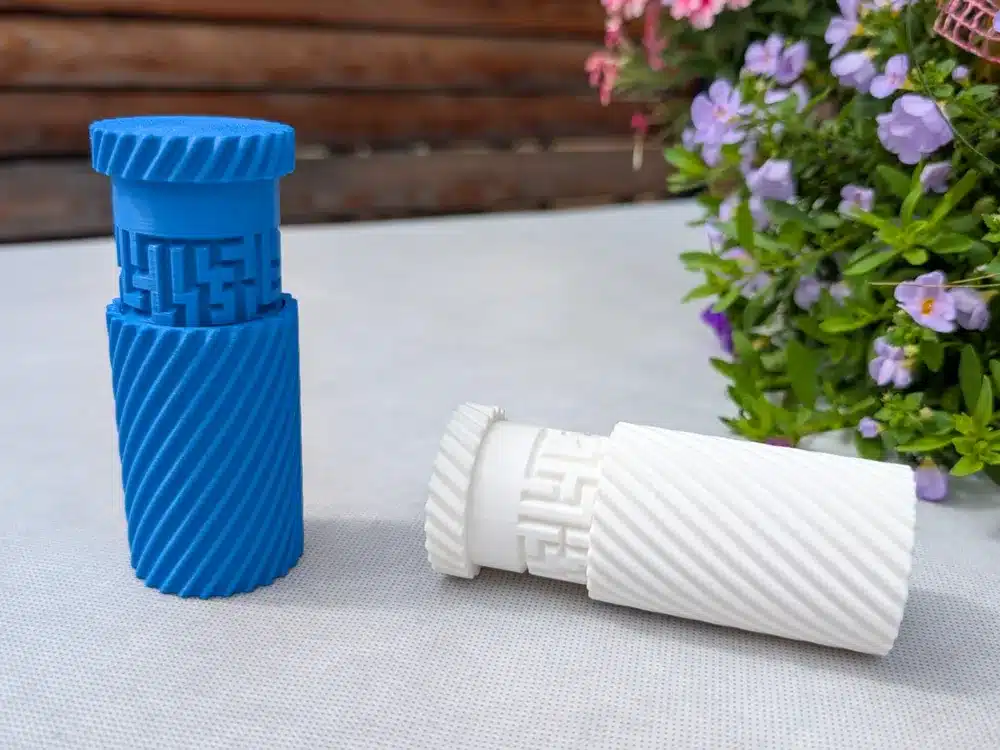 3D-printed blue and white cylindrical puzzles on a table, with colorful flowers in the background.