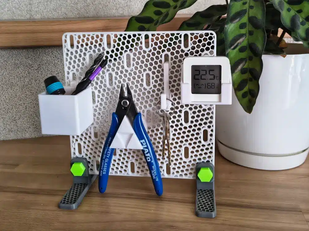 Pegboard organizer with tools, digital thermometer, and keys beside a potted plant on a wooden surface.