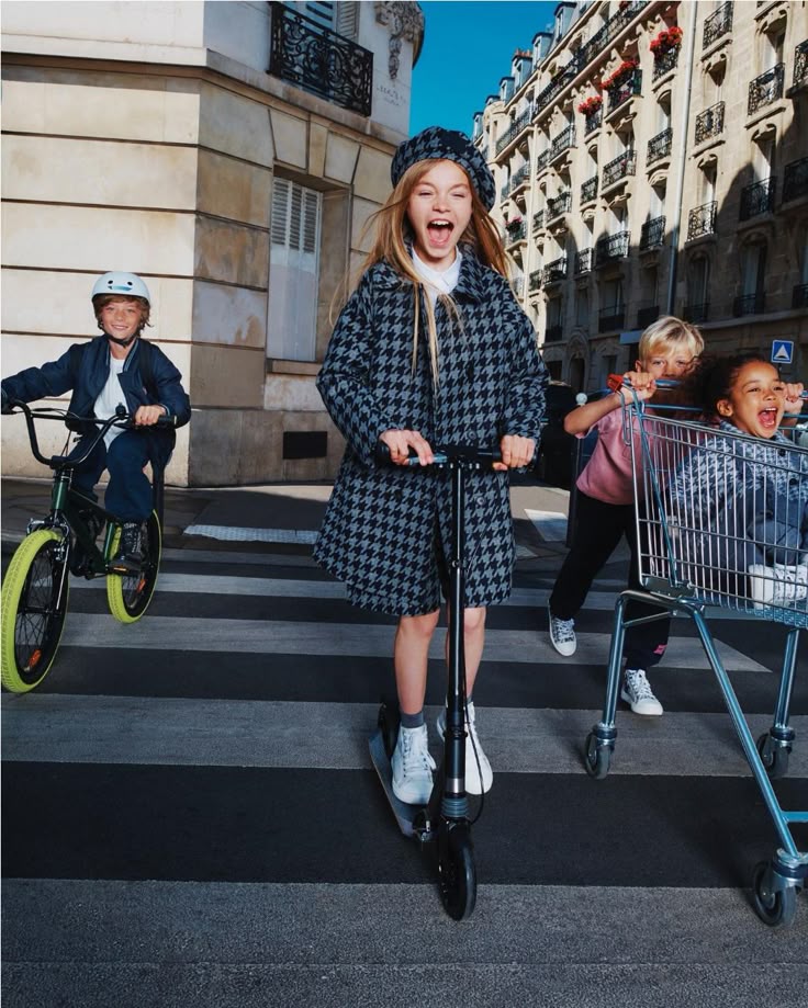 Kids having fun on a Paris street: girl on scooter, boy on bike, kids with shopping cart.