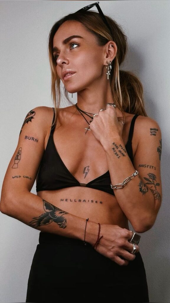 Tattooed woman in a black bralette and accessories, gazing to the side, showcasing bold body art and style.