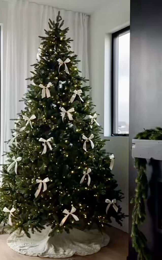 Elegant Christmas tree decorated with white bows and lights, standing in a cozy living room corner.