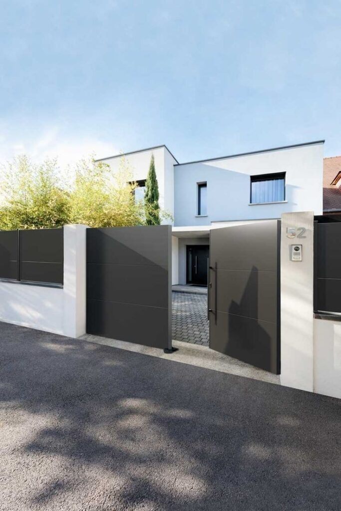 Modern white house with open gray gate, surrounded by trees, on a clear day.