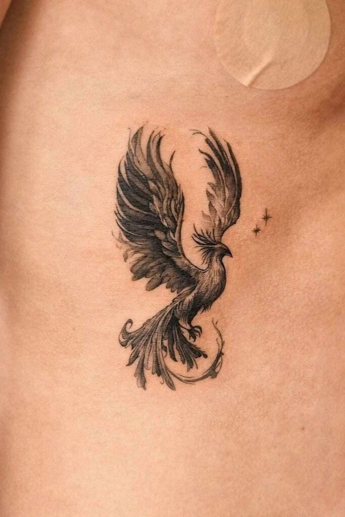 Elegant black phoenix tattoo on skin with wings spread, surrounded by small stars, symbolizing rebirth and strength.