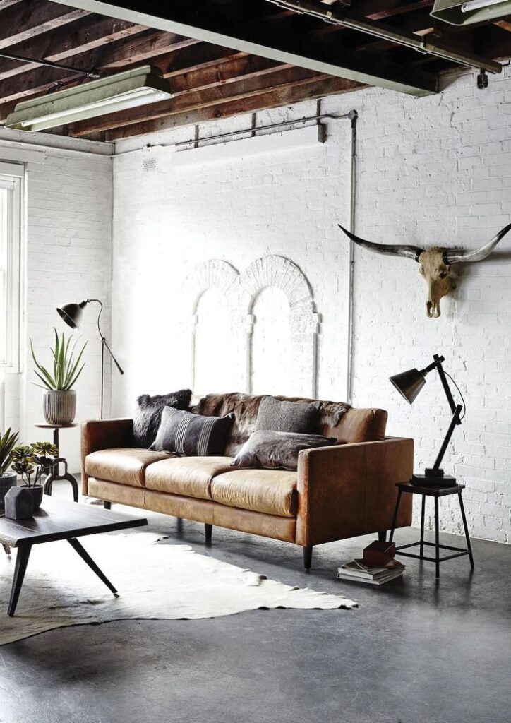 Industrial chic living room with leather sofa, wall-mounted skull, plants, and modern lighting on white brick walls.