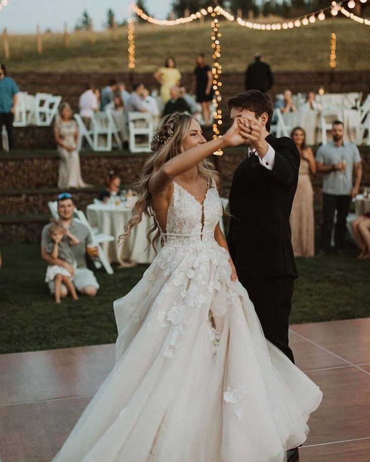 Bride and groom dancing at outdoor wedding with string lights and guests in the background.