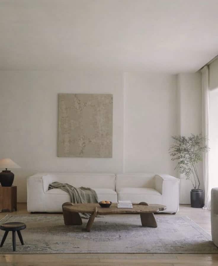 Minimalist living room with white sofa, wooden coffee table, neutral decor, and potted plant creating a serene atmosphere.