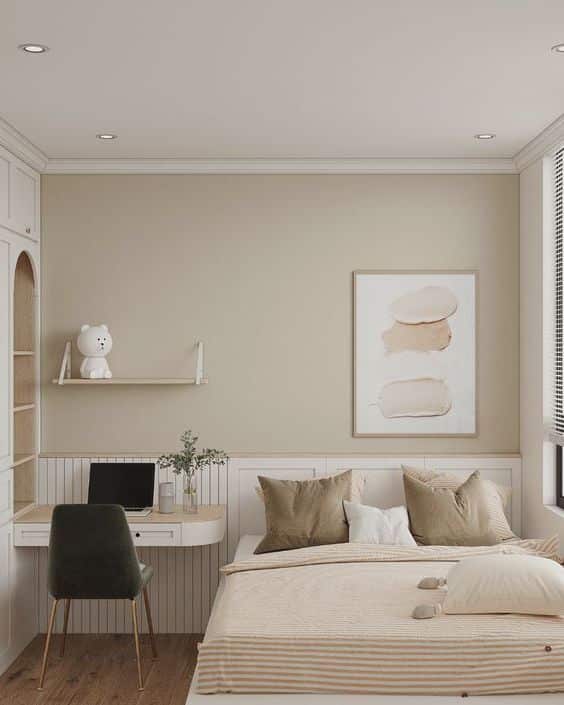 Minimalist bedroom with neutral tones, cozy bed, wall art, shelf, and small workspace with chair and laptop.
