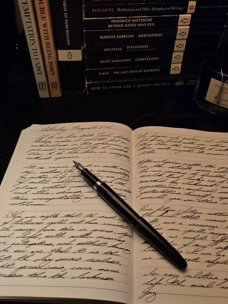Open notebook with handwritten text, black fountain pen, and stack of philosophy books in background.