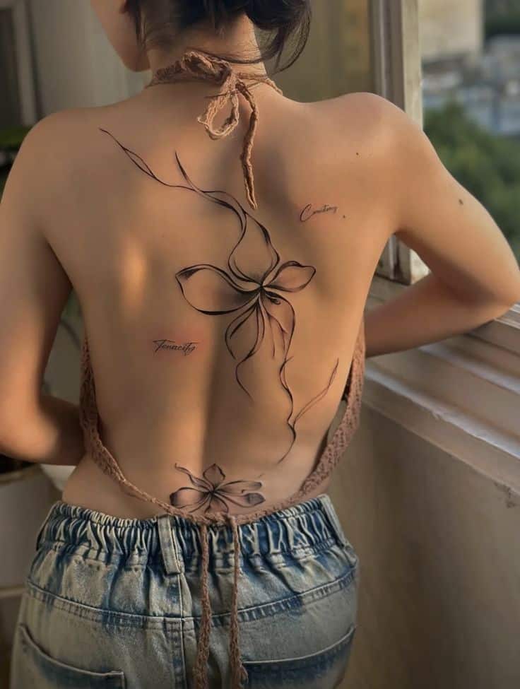 Back tattoo of floral design with words Creativity and Tenacity, on woman in halter top and jeans.