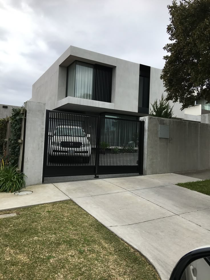 Modern two-story house with sleek concrete design, gated driveway, and landscaped front yard.