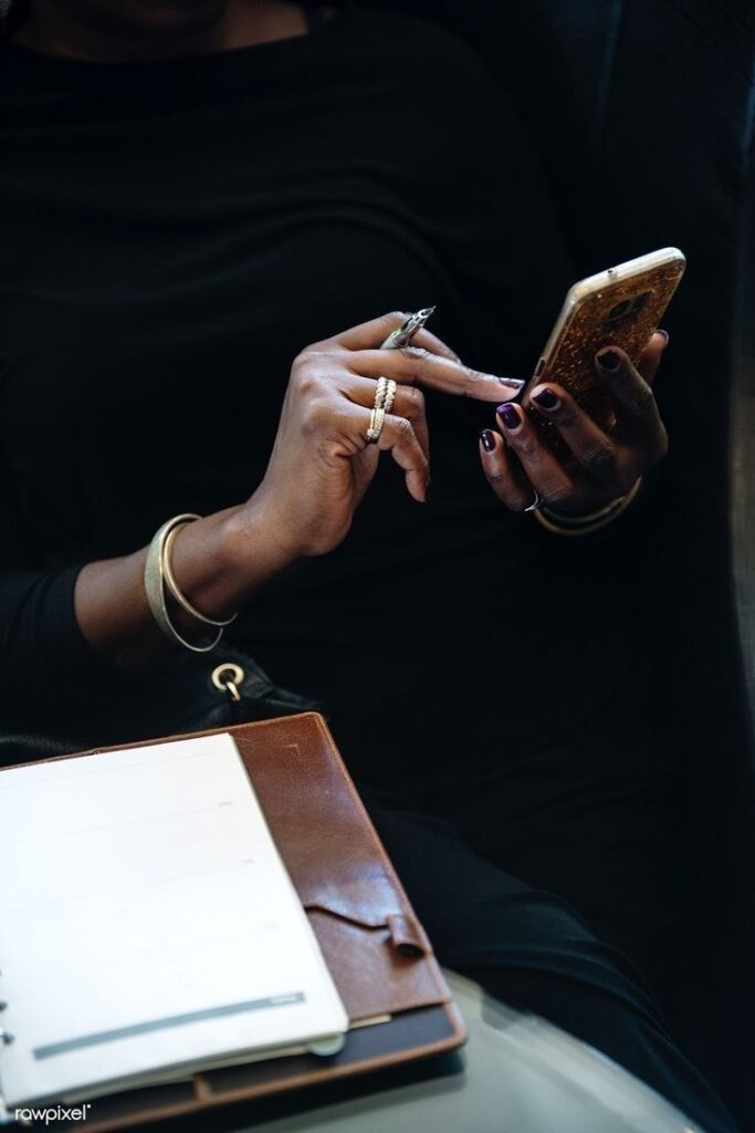 Person with rings using smartphone, next to a planner. Elegant, multitasking concept.