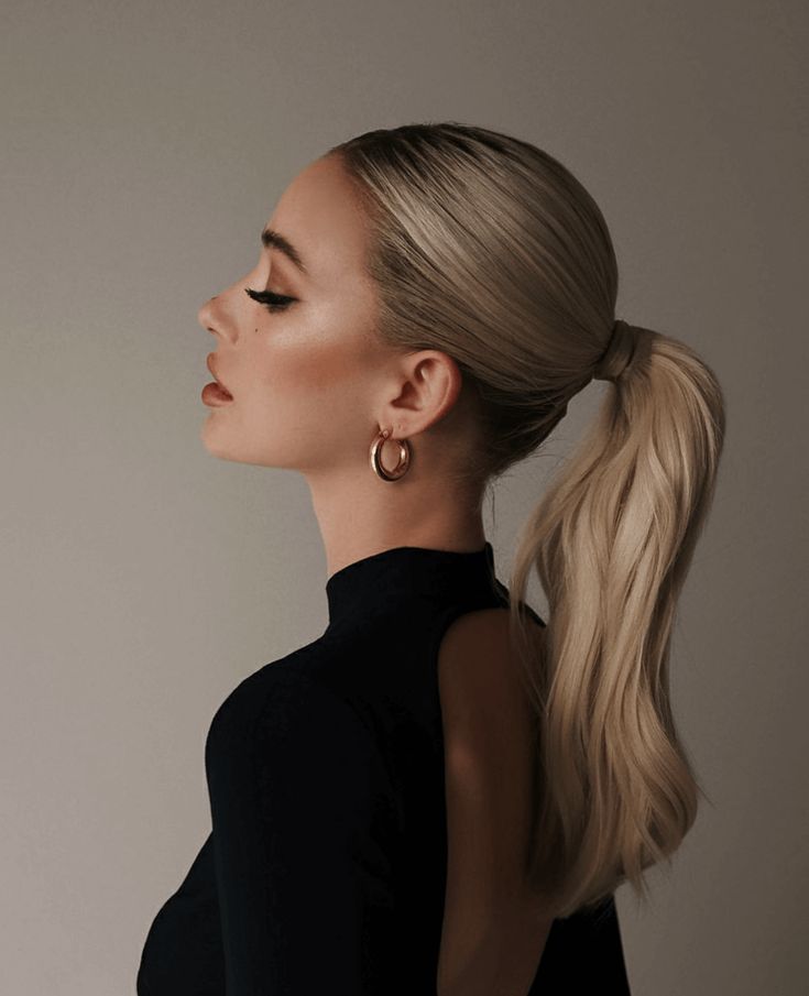 Woman with sleek ponytail and elegant black dress, wearing gold hoop earrings, side profile.