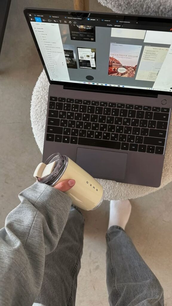 Person holding a cream tumbler next to laptop with design software open, standing on a stool.