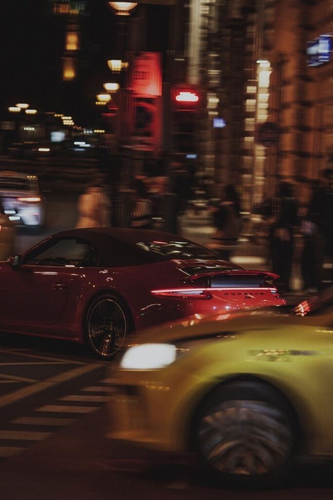 Red sports car speeds through a city street at night, blurred lights create a dynamic urban backdrop.