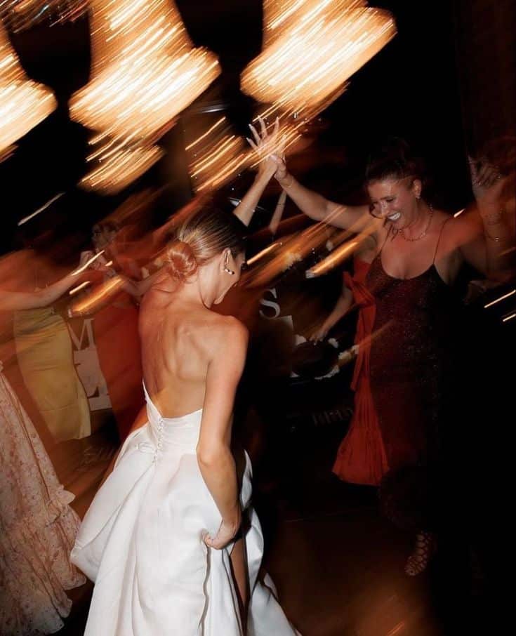 Elegant wedding celebration with guests dancing joyfully under warm lighting.