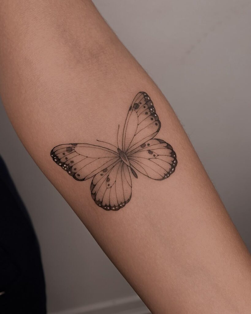 Black and grey butterfly tattoo on forearm, showcasing detailed wings and dotted patterns.