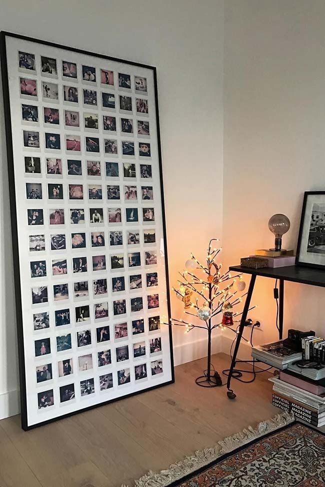 Wall art of Polaroid photos in frame, beside modern desk with books, small lit tree, and decorative light bulb.