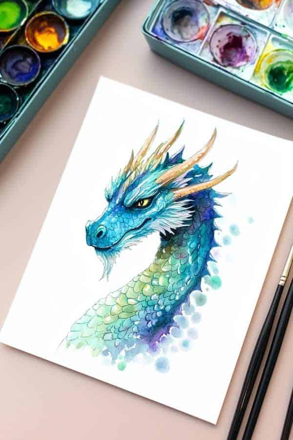 Watercolor dragon painting with vibrant blue and green scales beside art supplies.