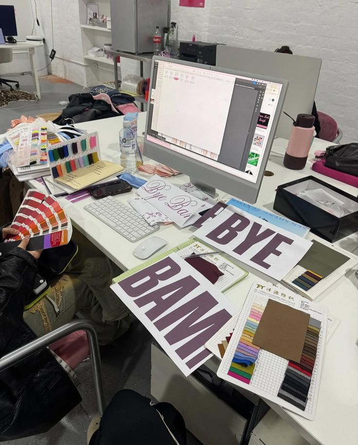 Design workspace with a computer, color samples, and fabric swatches for creative project planning.