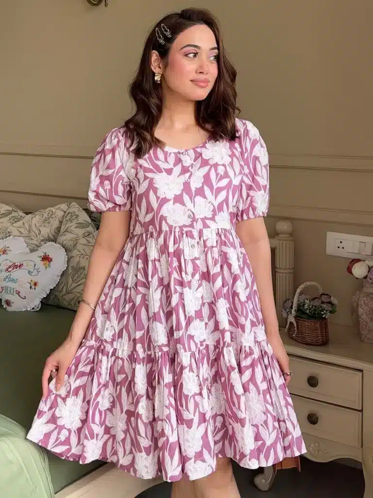 Woman in floral pink summer dress stands in a cozy room with vintage decor, looking to the side.