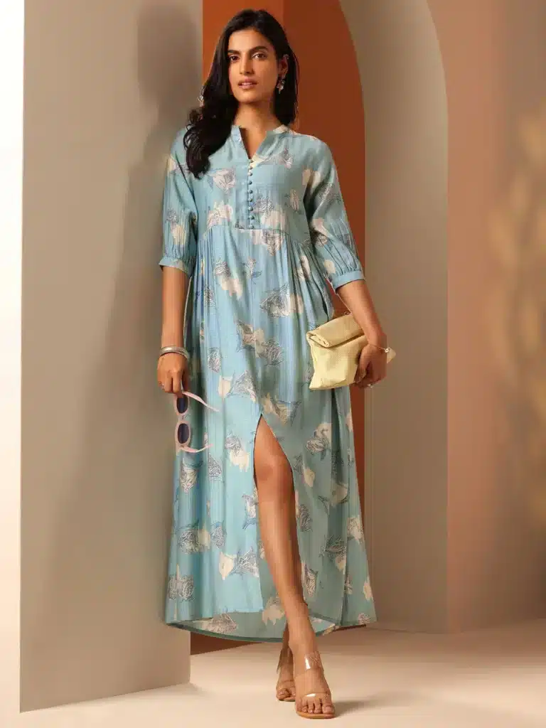 29780_6MAIN Woman in a stylish blue floral maxi dress holds sunglasses and a clutch in a modern, softly lit room. | Sky Rye Design Woman in a stylish blue floral maxi dress holds sunglasses and a clutch in a modern, softly lit room.