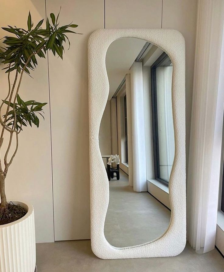 Curved full-length mirror in modern room with large windows and potted plant.