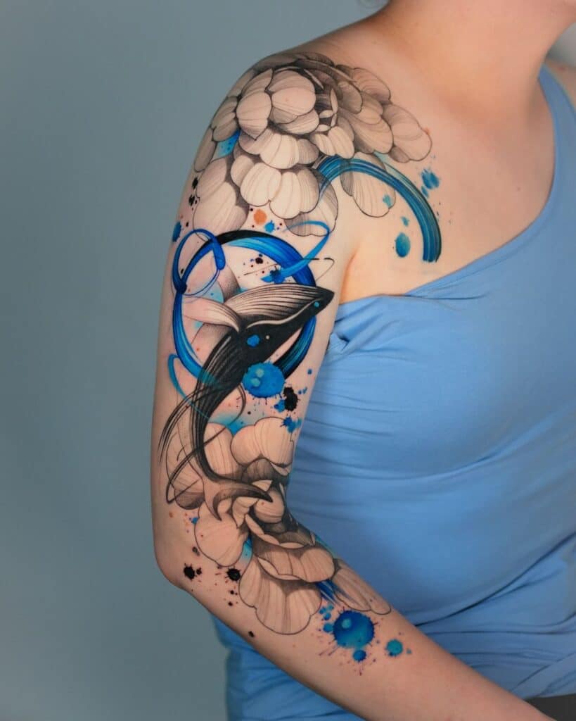 Abstract floral and whale tattoo on arm with blue and black ink, wearing a light blue top.
