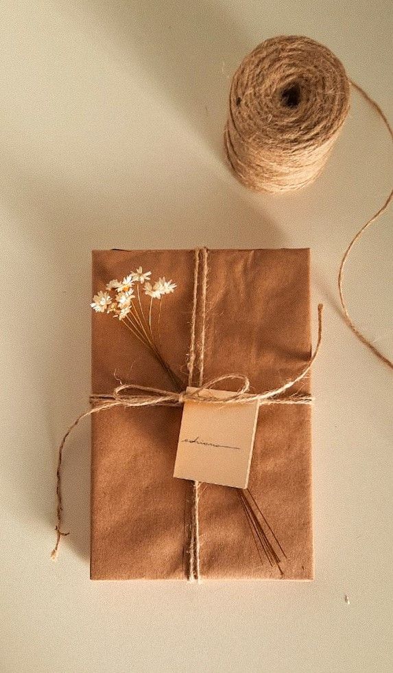 Rustic gift wrap with twine and dried flowers, accompanied by a roll of jute string on a light background.