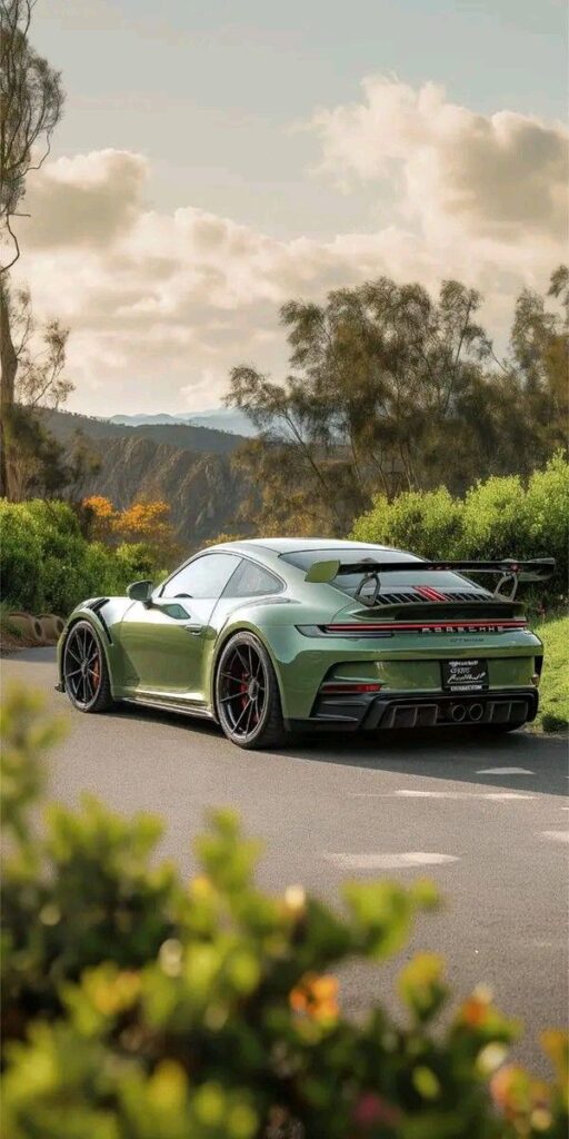 Green sports car on scenic road with mountain backdrop and clear sky.