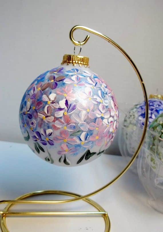 Hand-painted floral ornament on a golden stand, showcasing intricate purple and pink flowers.