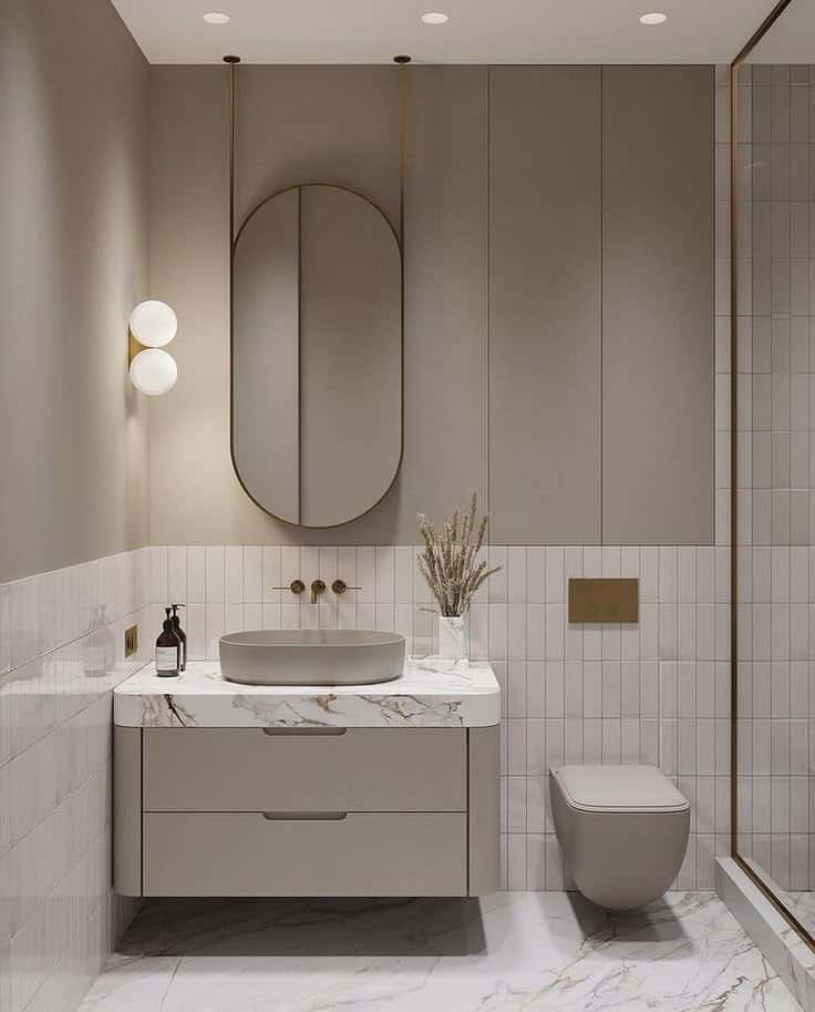 Modern bathroom with oval mirror, marble countertop, vessel sink, and wall-mounted fixtures. Minimalist design.