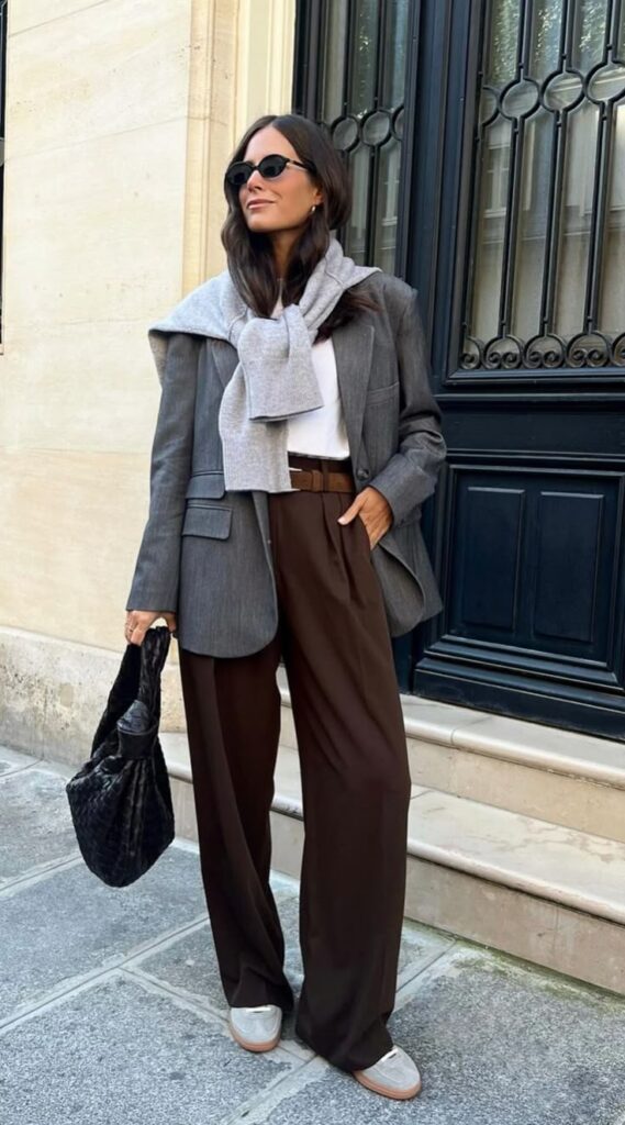 Stylish woman in sunglasses wearing a grey blazer, sweater, and brown pants stands in an urban setting. Autumn outfits