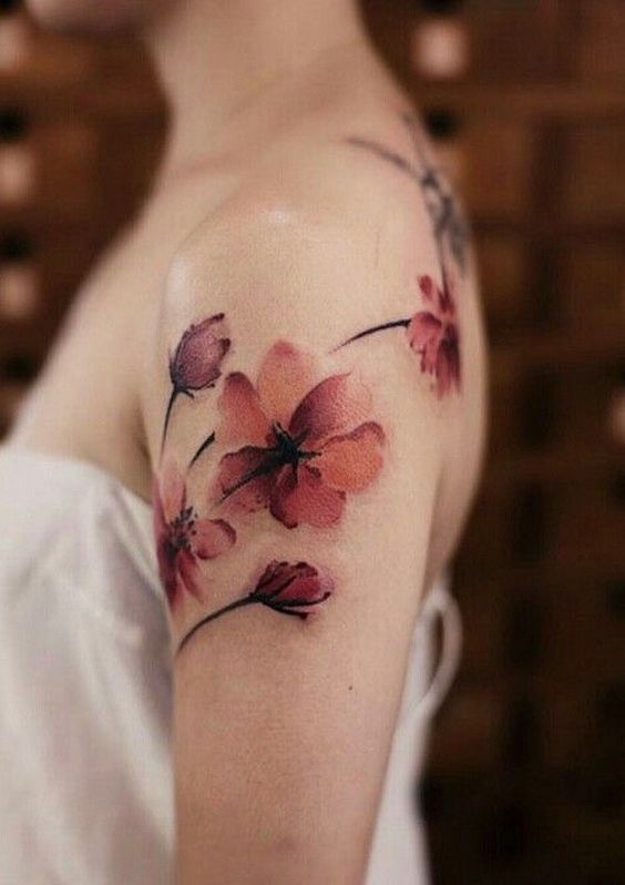 Delicate cherry blossom tattoo on woman's shoulder, showcasing intricate floral design and vibrant colors.