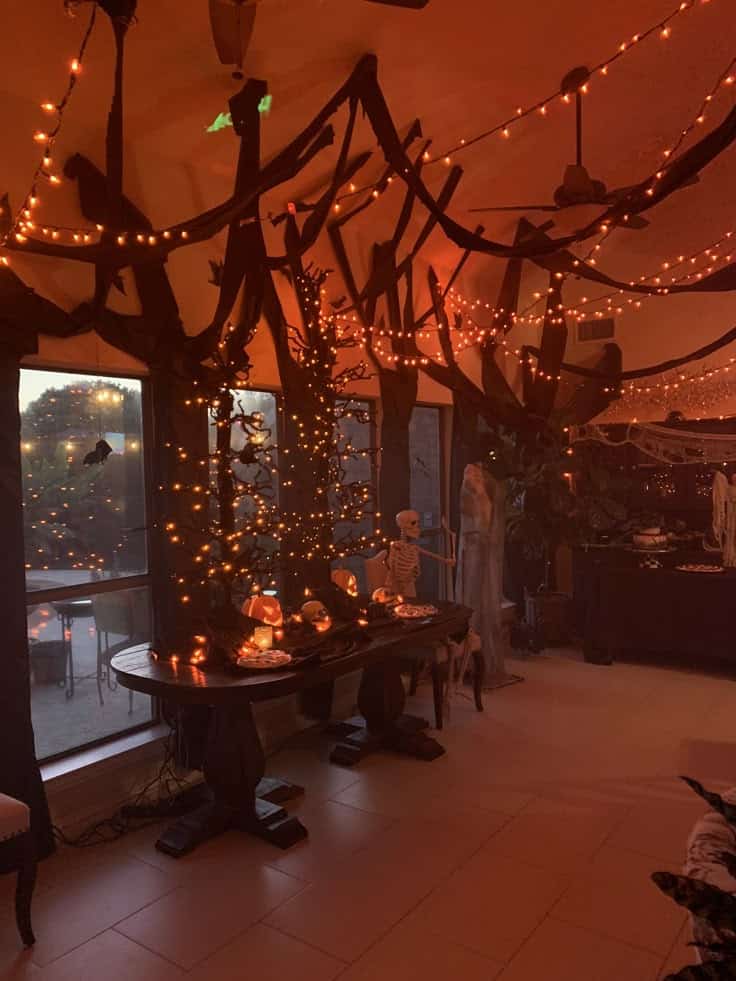 Halloween-themed room with orange string lights, pumpkins, skeleton, and spooky decorations for a festive atmosphere.