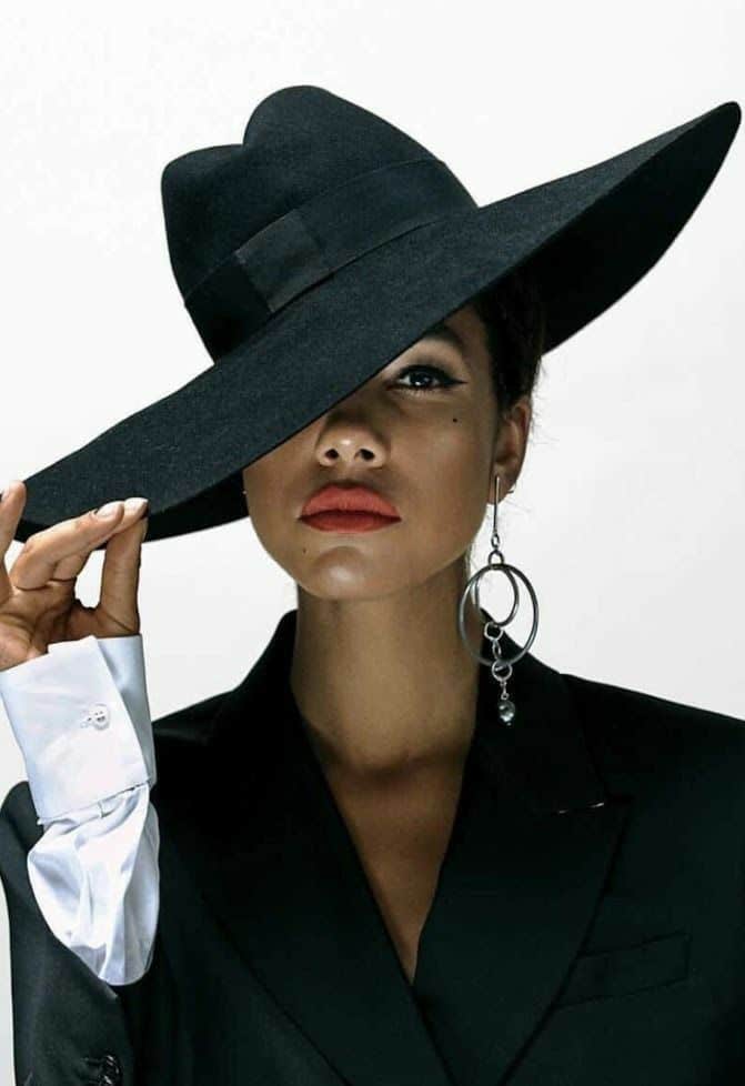 Stylish person in a black hat and earrings posing confidently, wearing a suit, with bold red lipstick. Inspiration photos