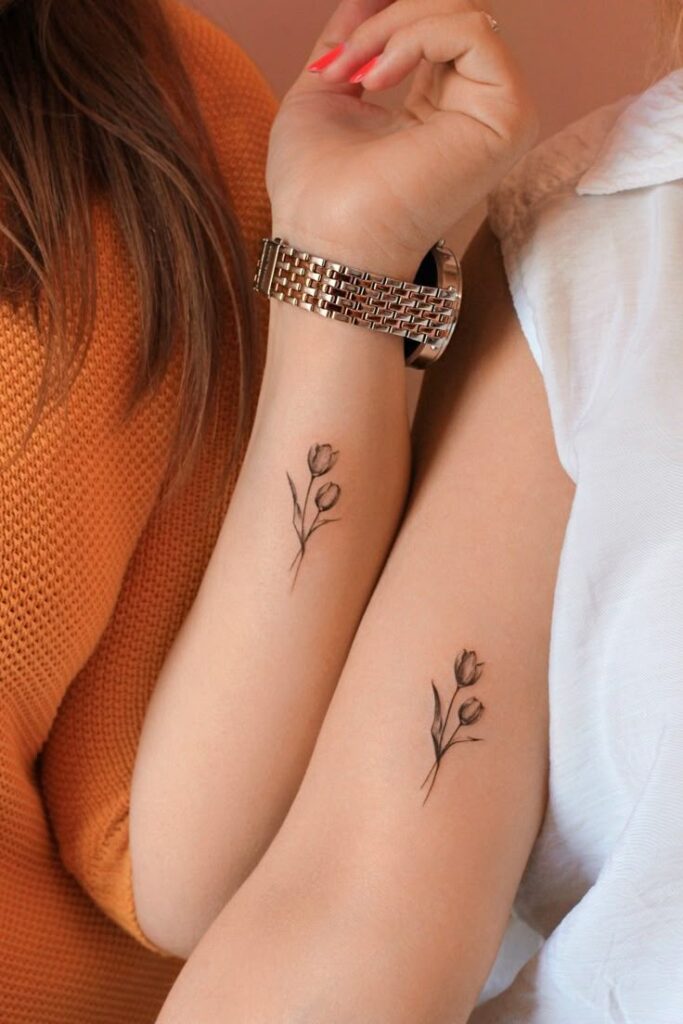 Matching floral tattoos on two arms, one with a watch. Minimalist black ink design.