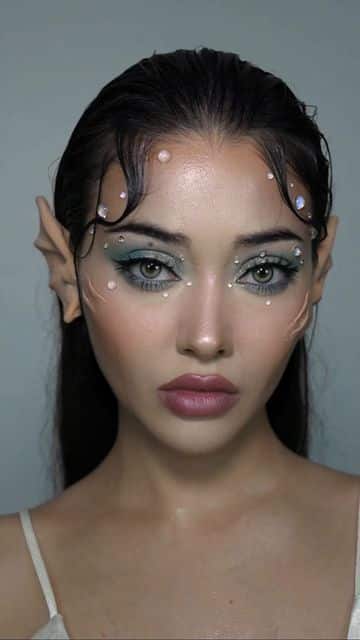 Fantasy-inspired makeup with elf ears, pearl accents, and bold eye makeup on model with long dark hair.