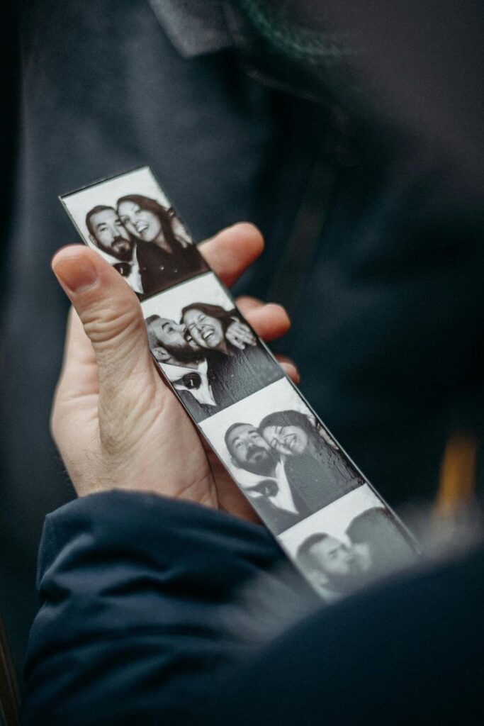 Person holding a strip of black and white photo booth images of a smiling couple.